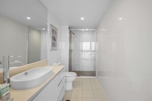 A modern bathroom with a large white sink, a toilet, and a glass-enclosed shower area.