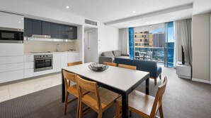 A modern hotel room with a kitchen, dining area, and a large window with a city view.