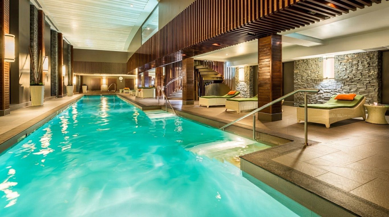 An indoor swimming pool with lounge chairs and a stone wall.