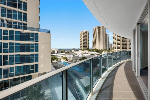 A modern building with a glass balcony overlooking a pool and other residential buildings.