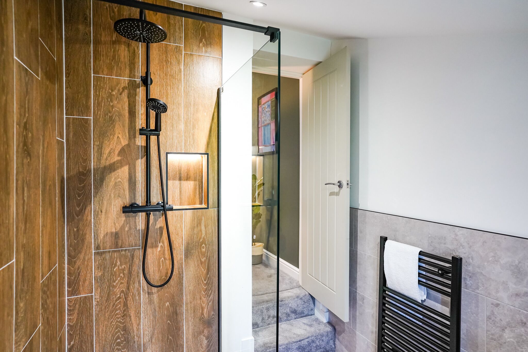 A modern bathroom with a glass shower enclosure, wooden flooring, and a towel rack.