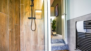 A modern bathroom with a wooden wall, a shower with a handheld showerhead, and a towel rack with a towel. - The City Centre Studios (Peterborough)