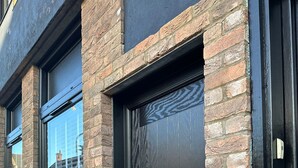 Una puerta negra con picaporte plateado, un buzón pequeño y una ventana que da a un edificio.