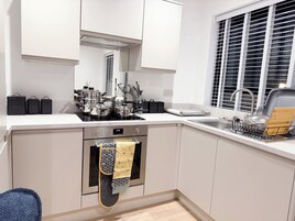 A modern kitchen with white cabinets, a built-in oven, and a window with blinds.