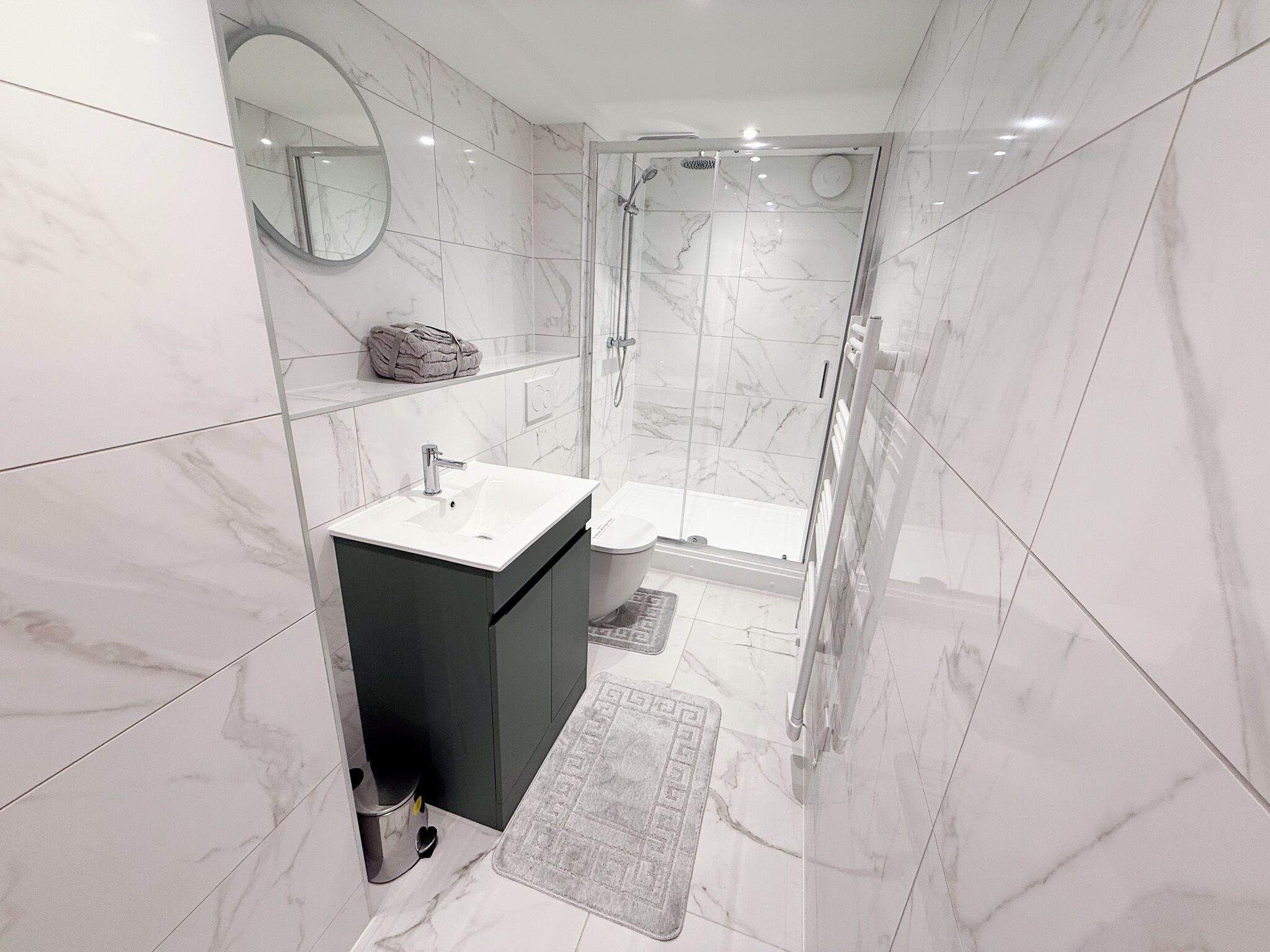 A modern bathroom with a marble floor, a sink with a mirror above it, a shower with a glass door, and a towel on the wall.
