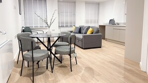 Una sala de estar moderna con un sofá gris, una mesa de comedor con sillas y una zona de cocina.