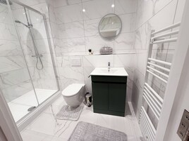A modern bathroom with a glass-enclosed shower, a toilet, a sink, and a towel rack.