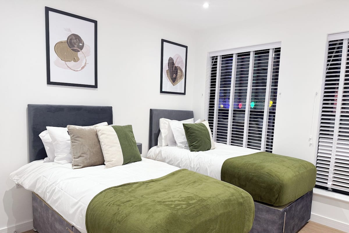 A double bed with a grey headboard, two bedside tables, and a green ottoman.