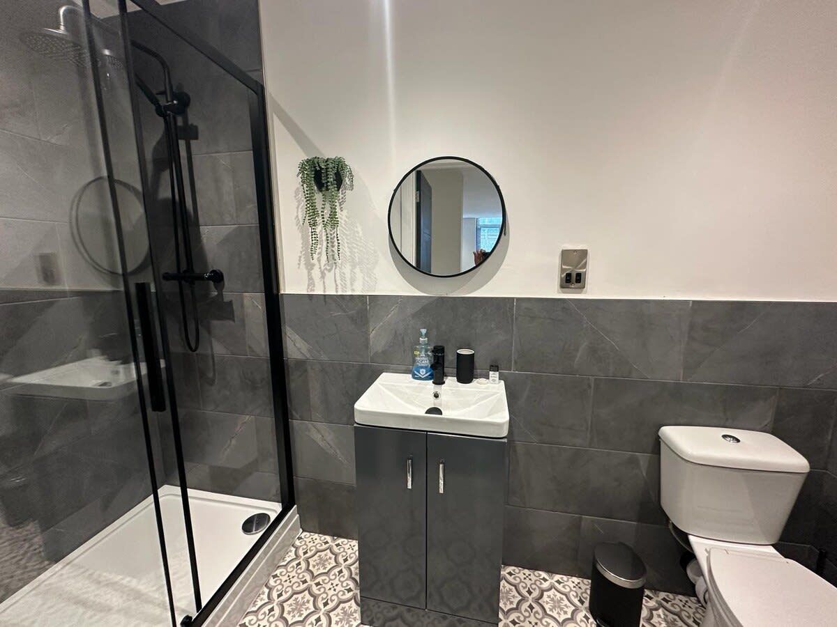 Un baño moderno con ducha de vidrio, un lavamanos blanco con un espejo encima y un inodoro.