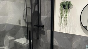 Un baño moderno con ducha de vidrio, lavamanos blanco y una planta decorativa.