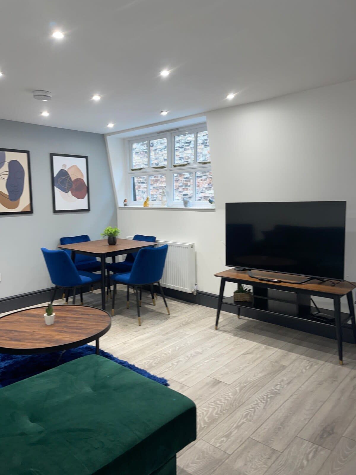 A modern living room with a dining area, a large flat-screen TV, and artwork on the walls.