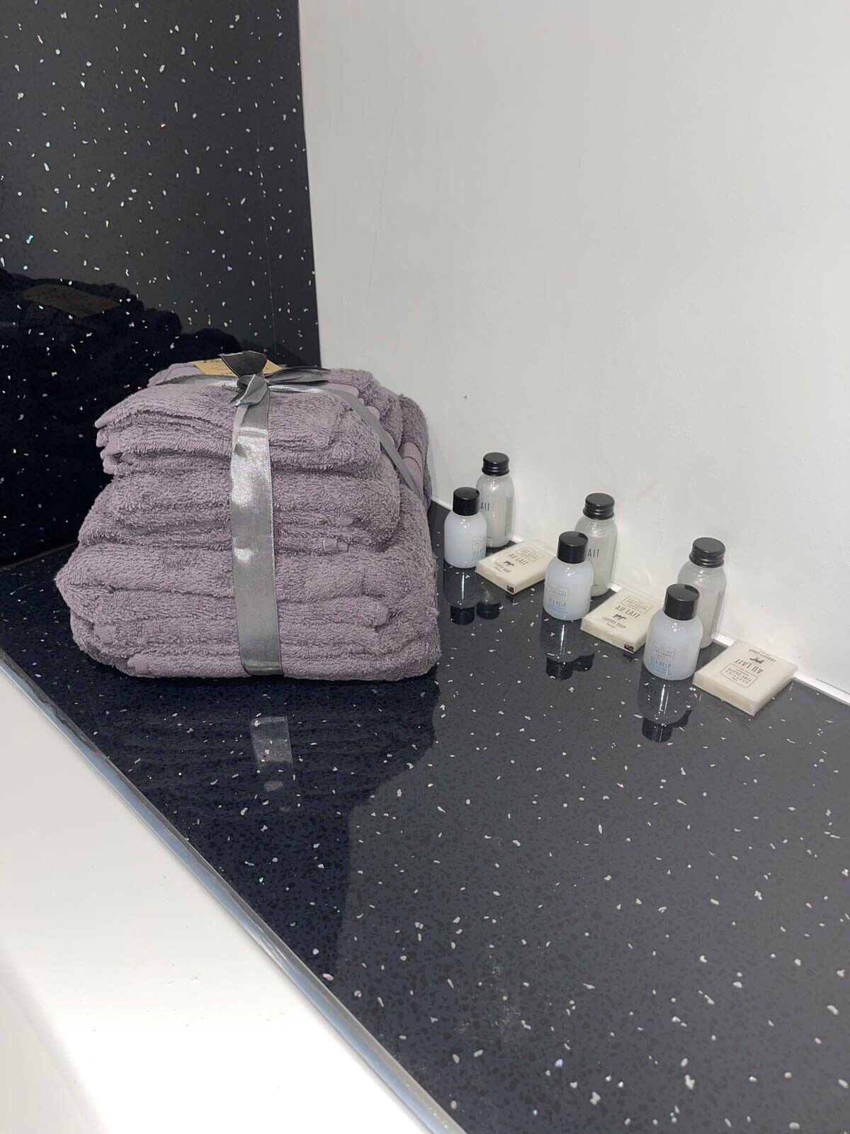 A bathroom with a stack of towels, a black countertop, and several bottles of toiletries.
