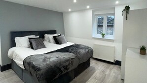A modern bedroom with a large bed, a window with plants, and a white dresser. - Abacus House Apartments (Huntingdon)