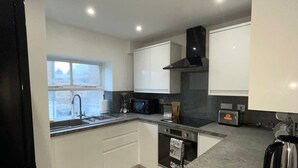 A modern kitchen with white cabinets, a black stove, a microwave, a toaster, and a kettle. - Abacus House Apartments (Huntingdon)