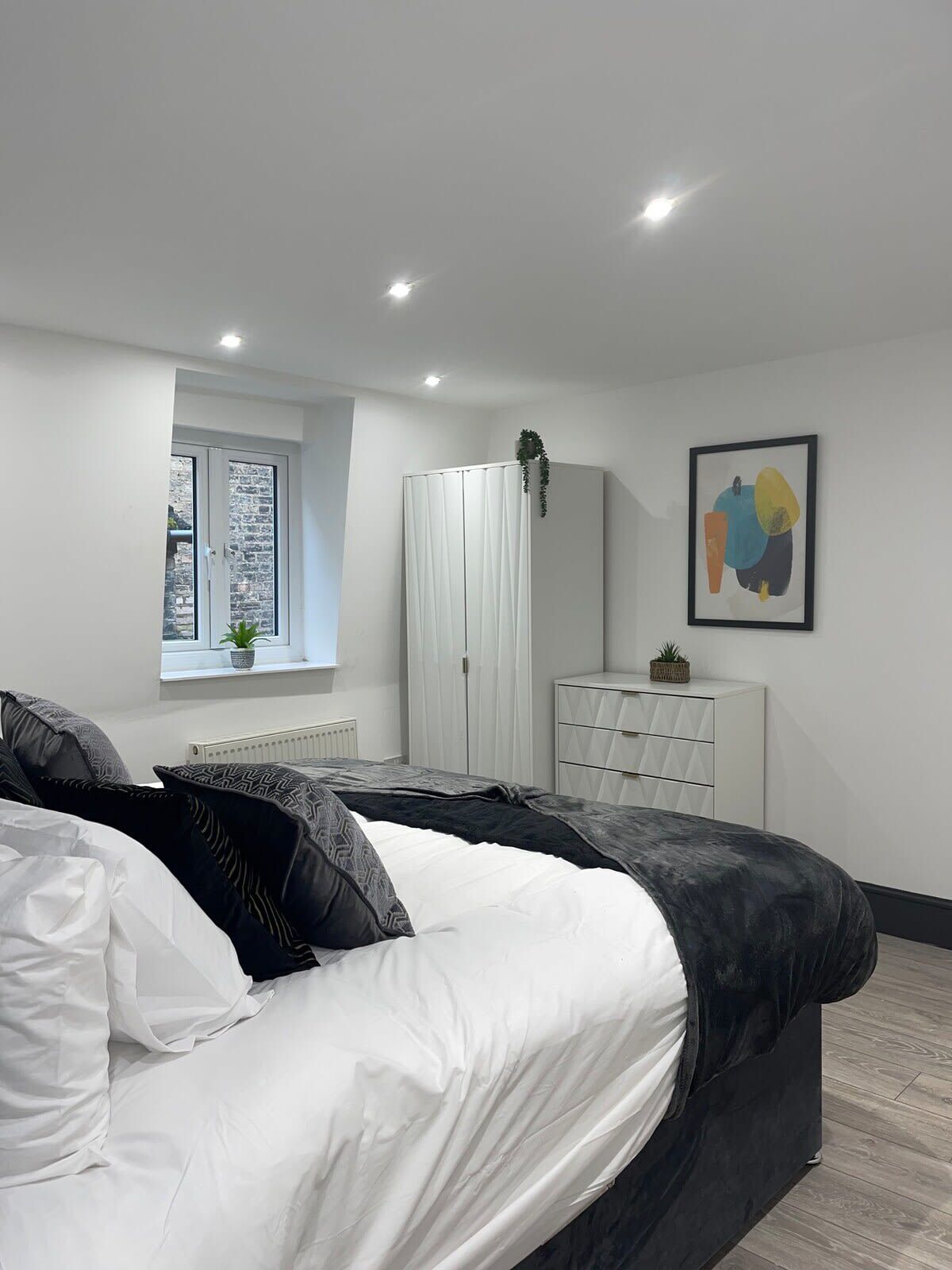 Een moderne slaapkamer met een bed, een garderobe, een dressoir en een raam met een plant.