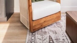 Un soggiorno moderno con un divano in legno, un tappeto decorato e arte astratta appesa al muro.
