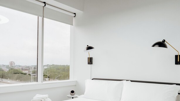 Camera d'albergo moderna con un letto grande, due lampade sui comodini, vista sulla città e una plafoniera circolare.