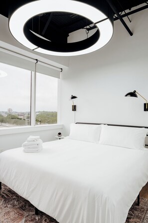 A modern hotel room with a large bed, two bedside lamps, a view of the city, and a circular ceiling light. - Four people. One Montgomery trip. Why split into hotel rooms? Stay together, keep your own space, and come back to Capitol views. (Montgomery)