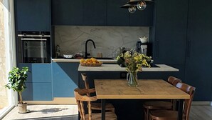 A modern kitchen with dark blue cabinets, a marble countertop, and a wooden dining table with chairs.