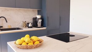 A modern kitchen with a marble countertop, a built-in induction cooktop, a coffee machine, and a basket of lemons.