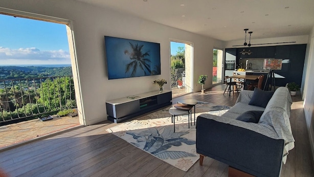 A spacious living area with a large window overlooking a scenic landscape, a modern kitchen, and a comfortable seating area.
