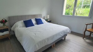 A bedroom with a bed, a nightstand, a chair, and a window with a view of greenery.