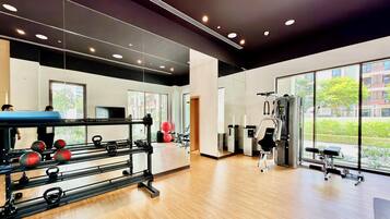 Un gimnasio con equipamiento de ejercicio, amplias ventanas y suelo de madera.