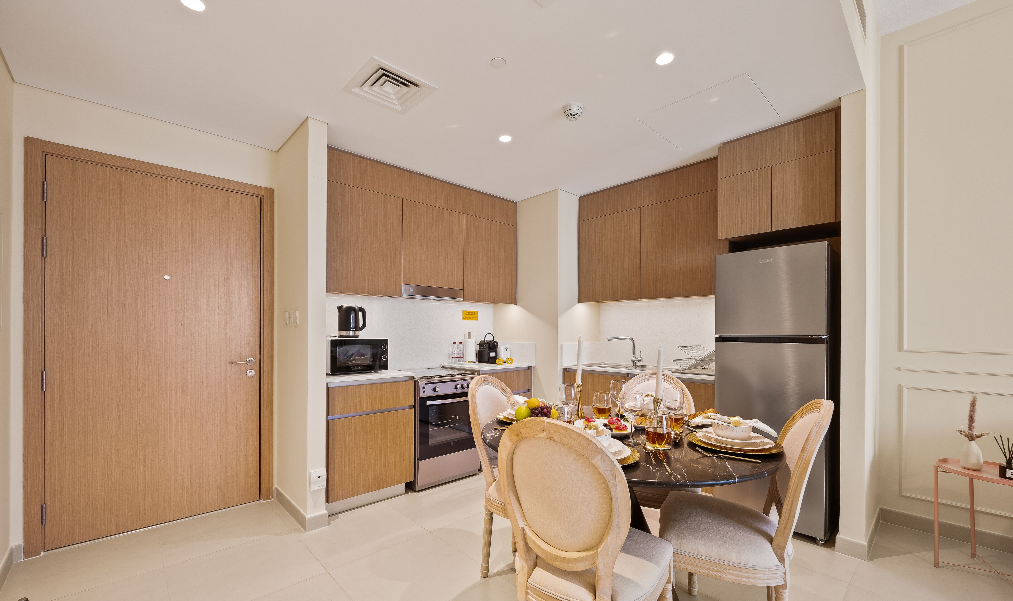 A modern kitchen with wooden cabinets, a stainless steel refrigerator, and a dining area with a round table and chairs.