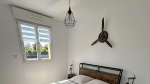 Ein Schlafzimmer mit Holzboden, einem Bett mit weißer Bettwäsche, einer Wanduhr und einem Fenster mit Jalousien.