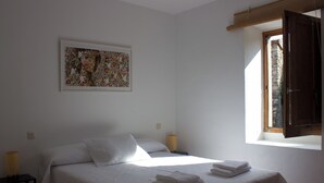 Ein Schlafzimmer mit Bett, Nachttisch, Lampe, Fenster mit Blick und einem gerahmten Bild an der Wand.