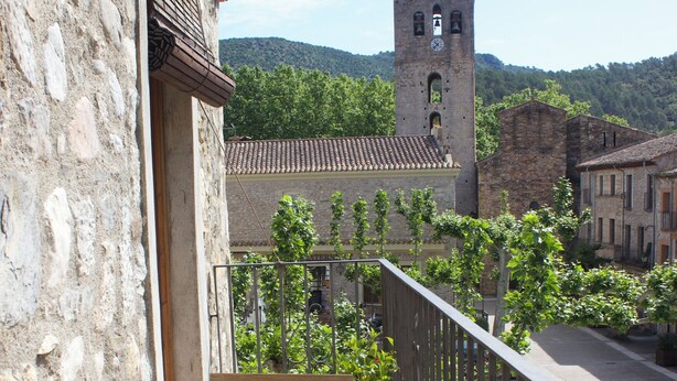 Ein Balkon mit hölzernen Bänken, ein Steinhaus und ein Turm im Hintergrund.