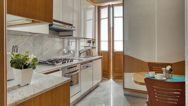 Una cucina moderna con piano cottura, forno e lavastoviglie integrati, pensili in legno e un'area pranzo con tavolo e sedie.