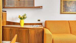 Una stanza con un armadio in legno, un vaso giallo con fiori, una rivista e un divano arancione.