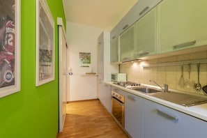 Eine kompakte Küche mit Mikrowelle, Herd und Spüle, sowie eine grüne Wand mit einem gerahmten Poster.