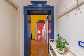 Un couloir avec un plancher en bois, une porte à cadre bleu et un mur blanc orné d’une plante.