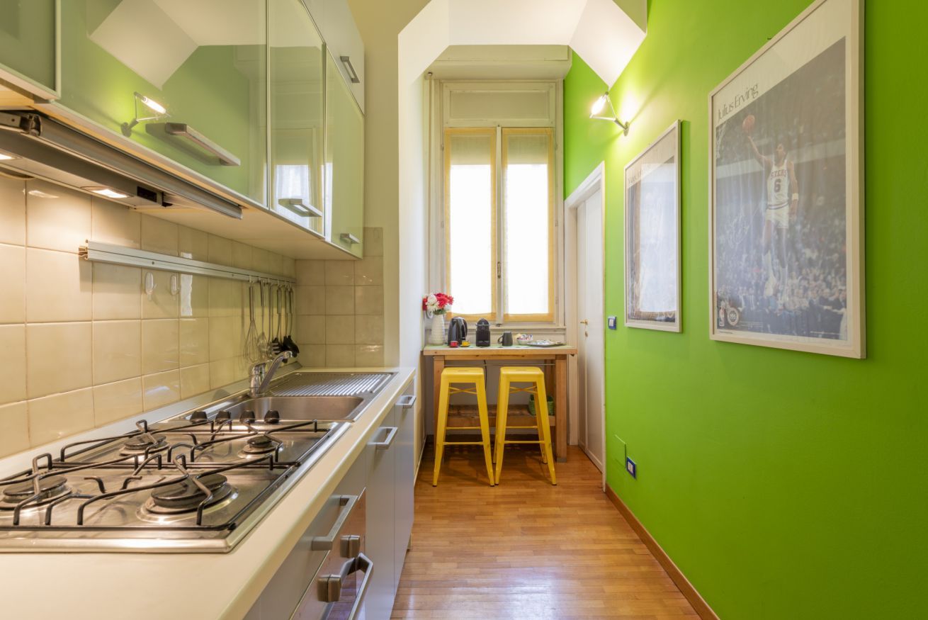 A kitchen with a gas stove, wooden stools, and framed pictures on the wall.