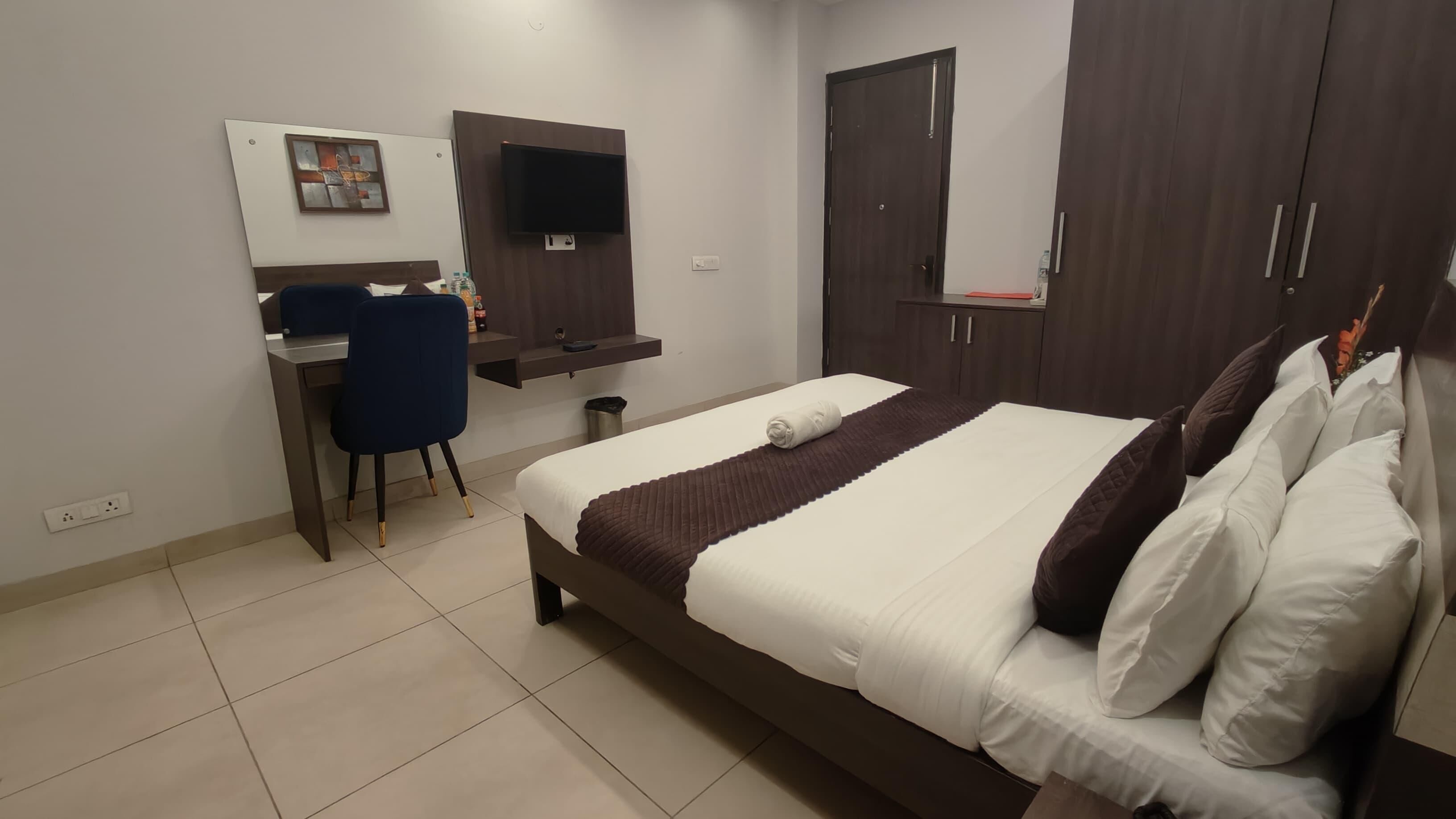 A hotel room with a bed, a desk, a chair, a TV, and a wardrobe.