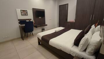 A hotel room with a bed, a desk, a chair, a TV, and a wardrobe.