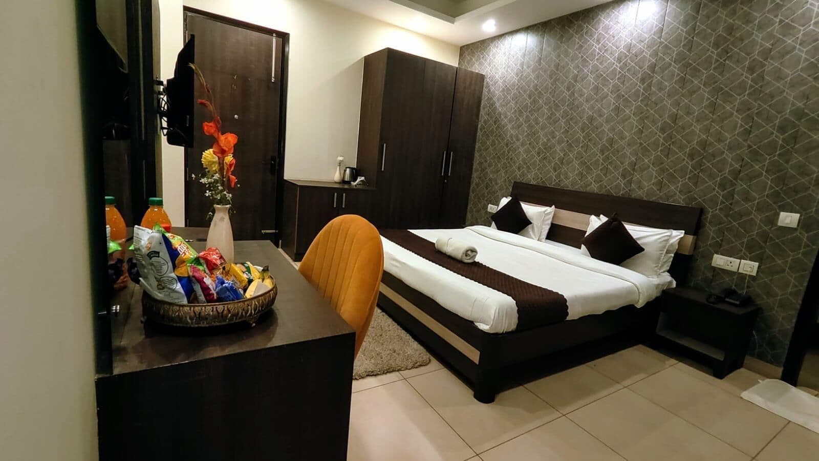 Una habitación de hotel con cama, escritorio con cesta de aperitivos, silla, armario y espejo.