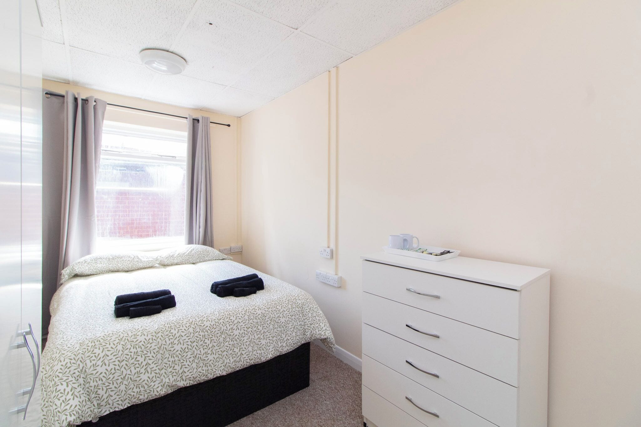 A bedroom with a bed, a dresser, and a window with curtains.