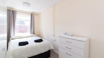 A bedroom with a bed, a dresser, and a window with curtains.