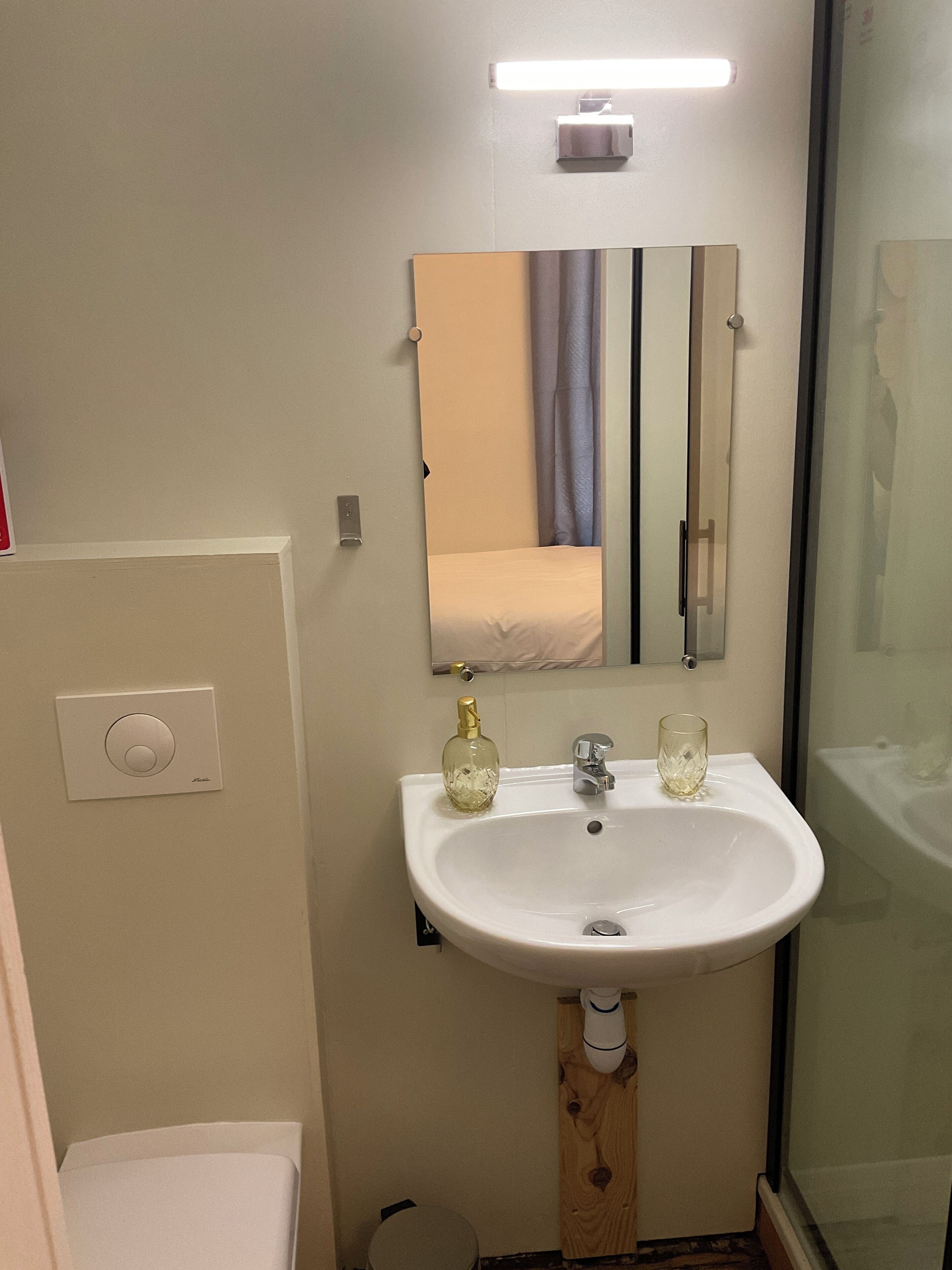 Un baño con lavamanos blanco, un espejo, toallero y un inodoro.