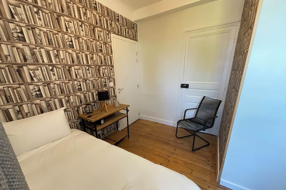 Un dormitorio con una cama grande, una mesita de noche de madera, una silla y una pared decorada con cuadros.