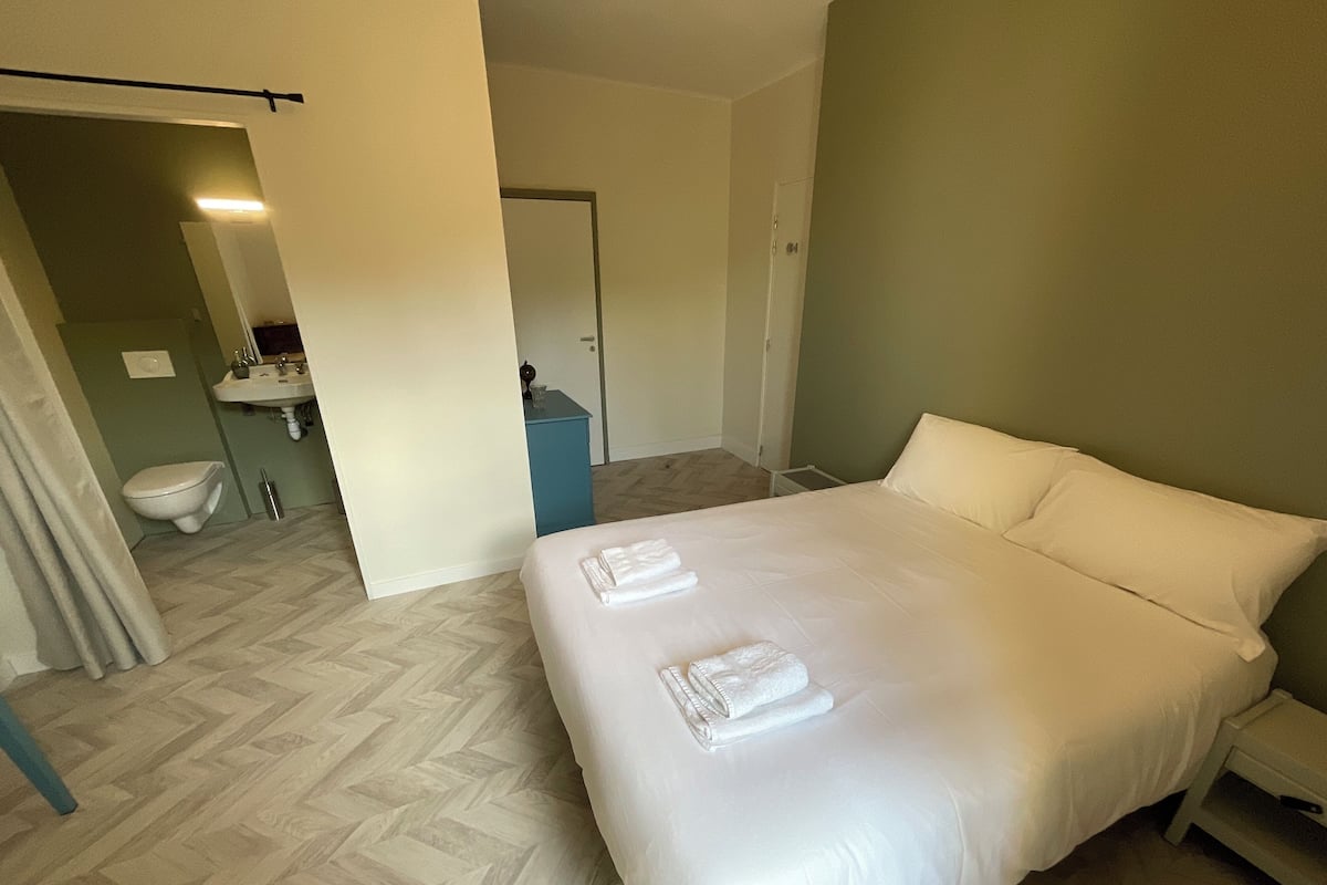 Habitación de hotel con una cama grande, una mesita de noche, baño con lavabo e inodoro, y un espejo.