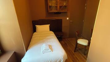 Une petite chambre à coucher accueillante, avec un lit simple, un plancher en bois, une armoire aux portes vitrées et une chaise.
