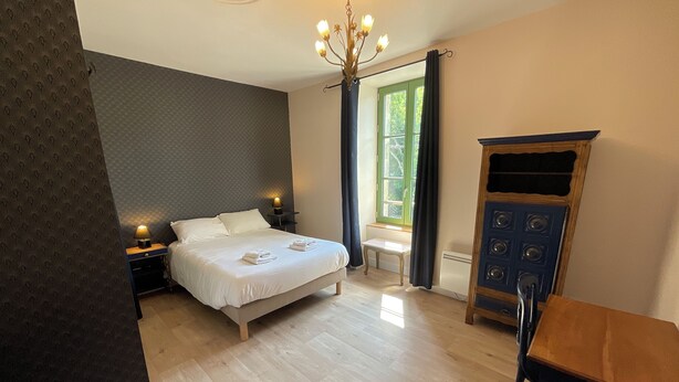 A bedroom with a bed, bedside tables, a chandelier, a window with curtains, a radiator, and a wooden cabinet. - TAVARN TY GAR (Hennebont)