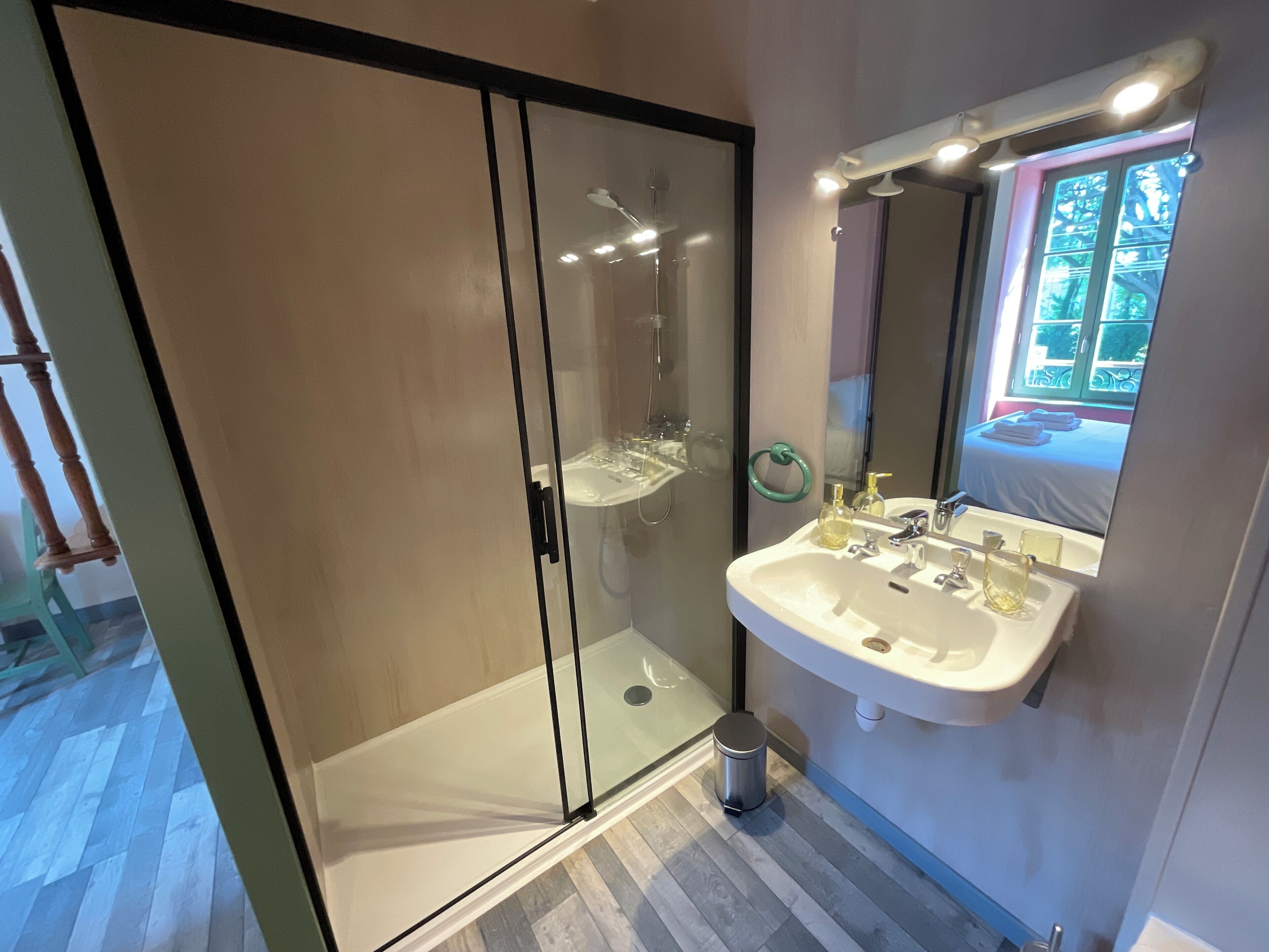 Ein modernes Badezimmer mit einer gläsernen Dusche, einem weißen Waschbecken und einem Spiegel mit Blick aus dem Fenster.