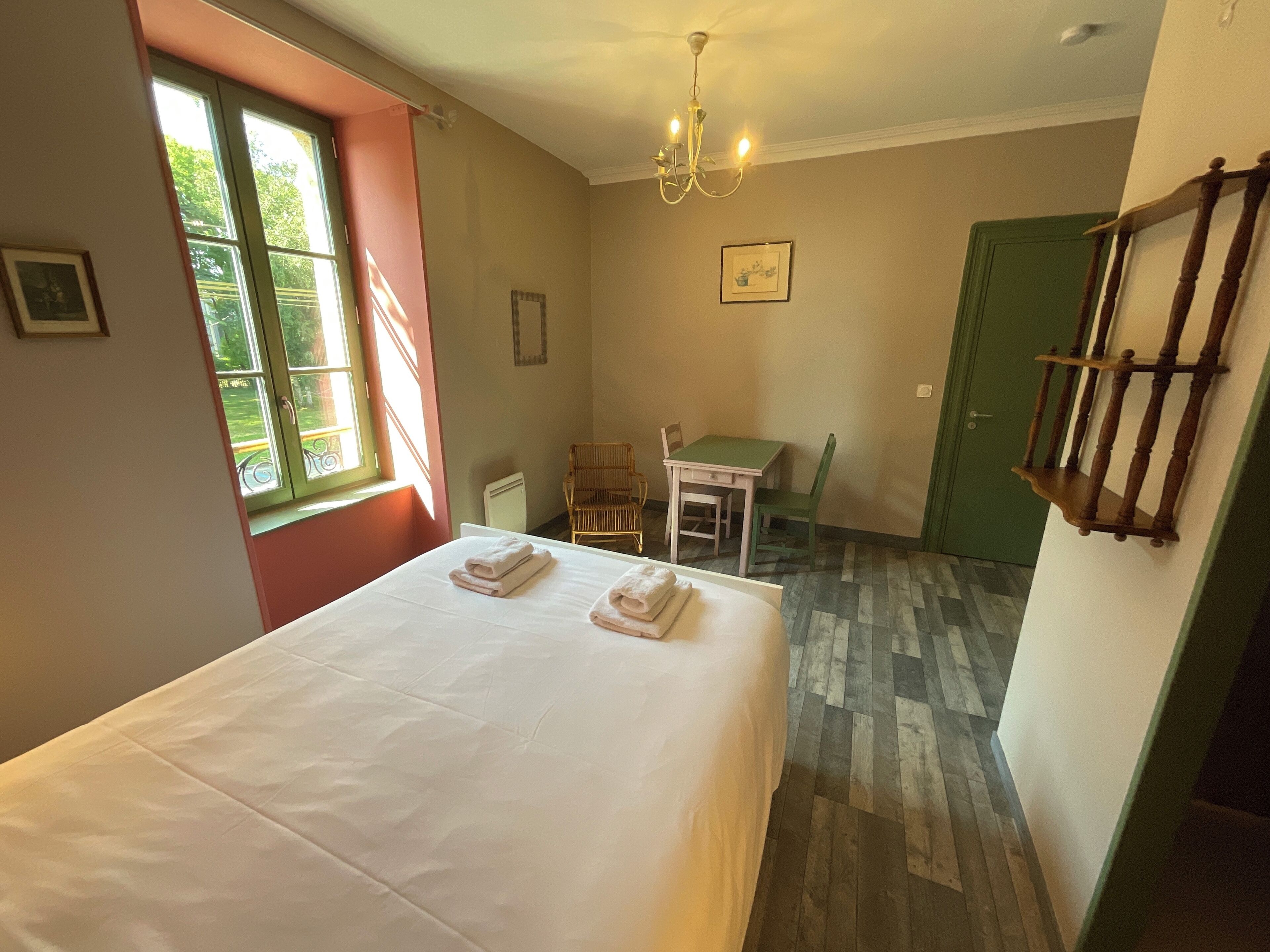Une chambre d’hôtel avec un lit, un bureau et une chaise. Il y a une fenêtre donnant sur un paysage verdoyant.