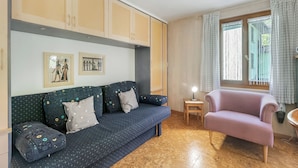 Un soggiorno con un divano blu scuro, una poltrona rosa chiaro, armadietti in legno e un tavolino con una lampada.
