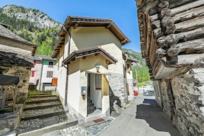 Una calle estrecha con edificios de piedra, una escalera de madera y montañas al fondo.